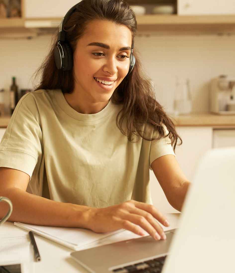 junge Frau mit braunen Haaren und Kopfhörern, tippend am Labtop, lächelt