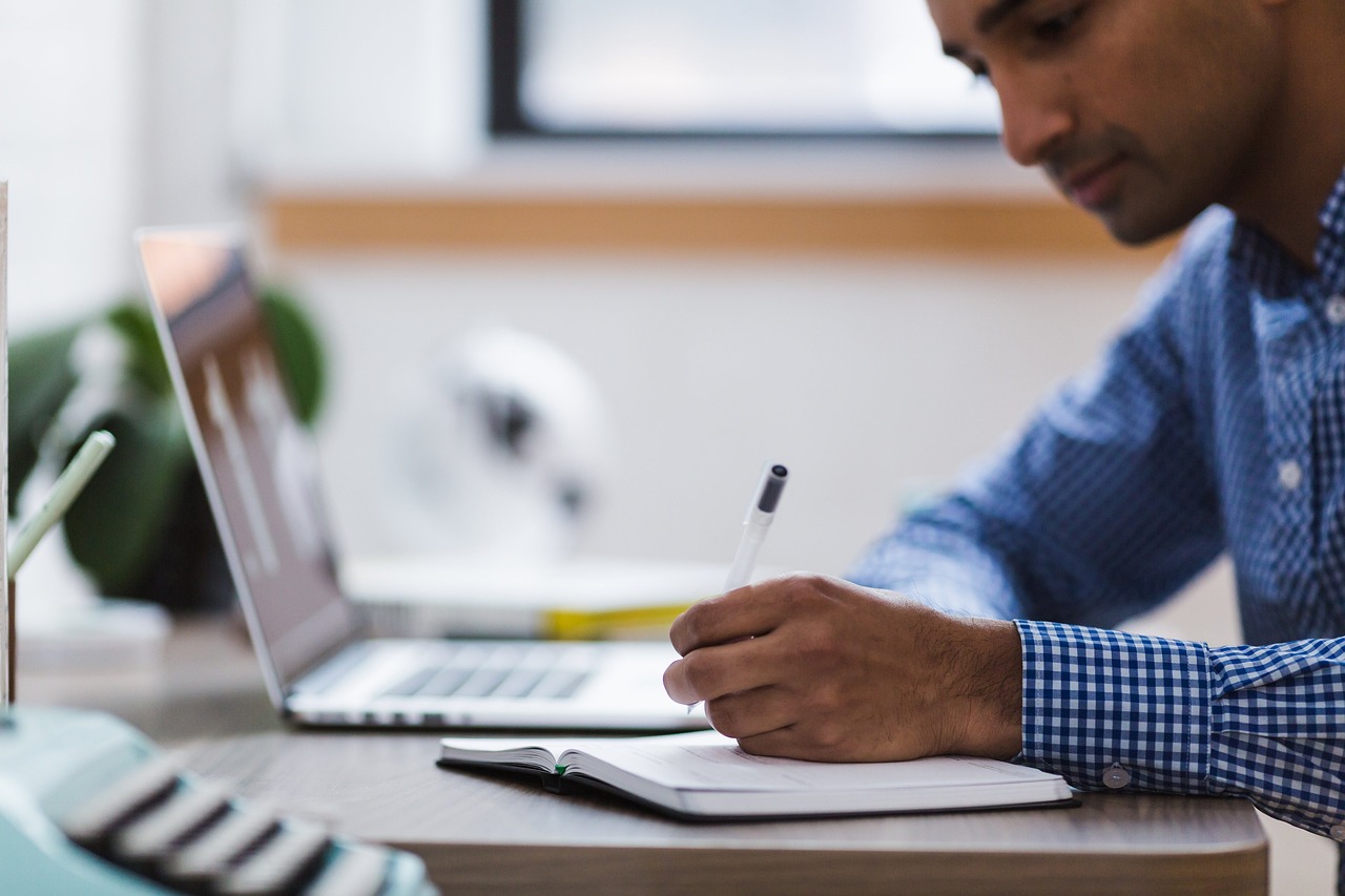 DUH-IT Lern-Center Mann an Laptop schreibt in ein Notizbuch